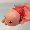 A hand is holding a pink and red clockwork animal bath toy with a round body and large eyes.