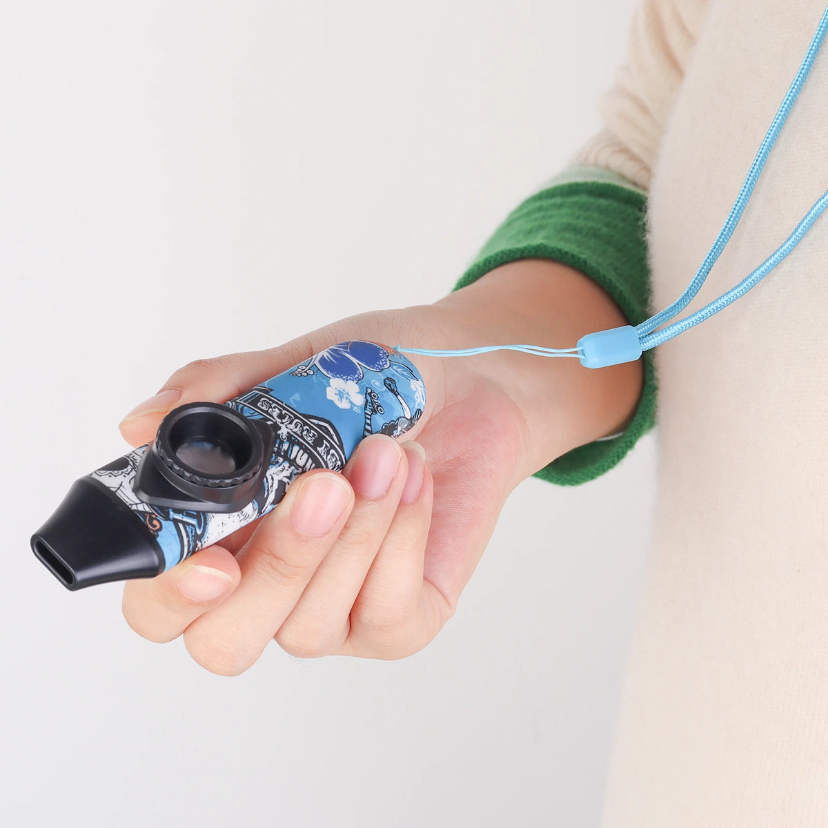 A hand holds an adjustable tone kazoo with a blue and white design and a light blue lanyard.