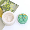 A light green silicone mold shaped like baby feet with small gold accents, next to a white container and a green leaf backgro