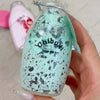 A hand holds a clear bottle filled with a light green liquid and dark specks, labeled Chiboki drink cup toy.