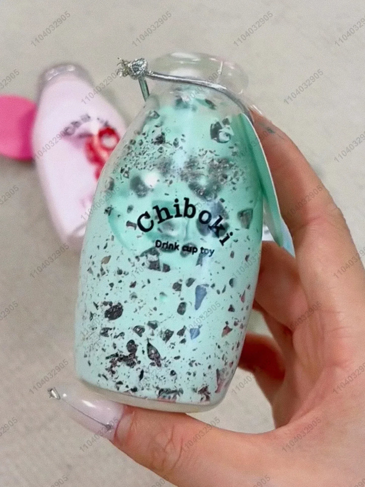 A hand holds a clear bottle filled with a light green liquid and dark specks, labeled Chiboki drink cup toy.