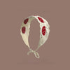 A white crochet headband decorated with red strawberry shapes on a neutral background.
