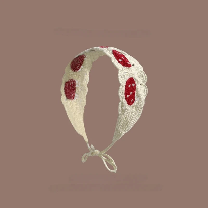 A white crochet headband decorated with red strawberry shapes on a neutral background.
