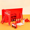 A red wooden fire brigade play set featuring an archway, ladder, and accessories on an orange surface.