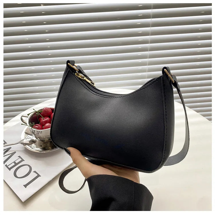 A black PU square crossbody bag with a gold zipper closure resting on a white surface.