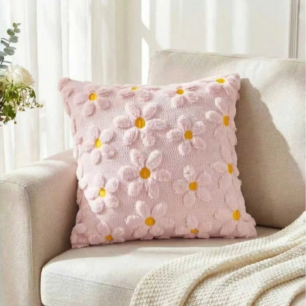 A pink faux fur pillow cover with embroidered yellow daisy designs resting on a light-colored sofa.