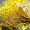 A pile of holographic gold glitter powder scattered across a dark surface.