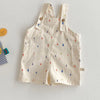 Cream colored kids overalls with a colorful raindrop print and wooden buttons