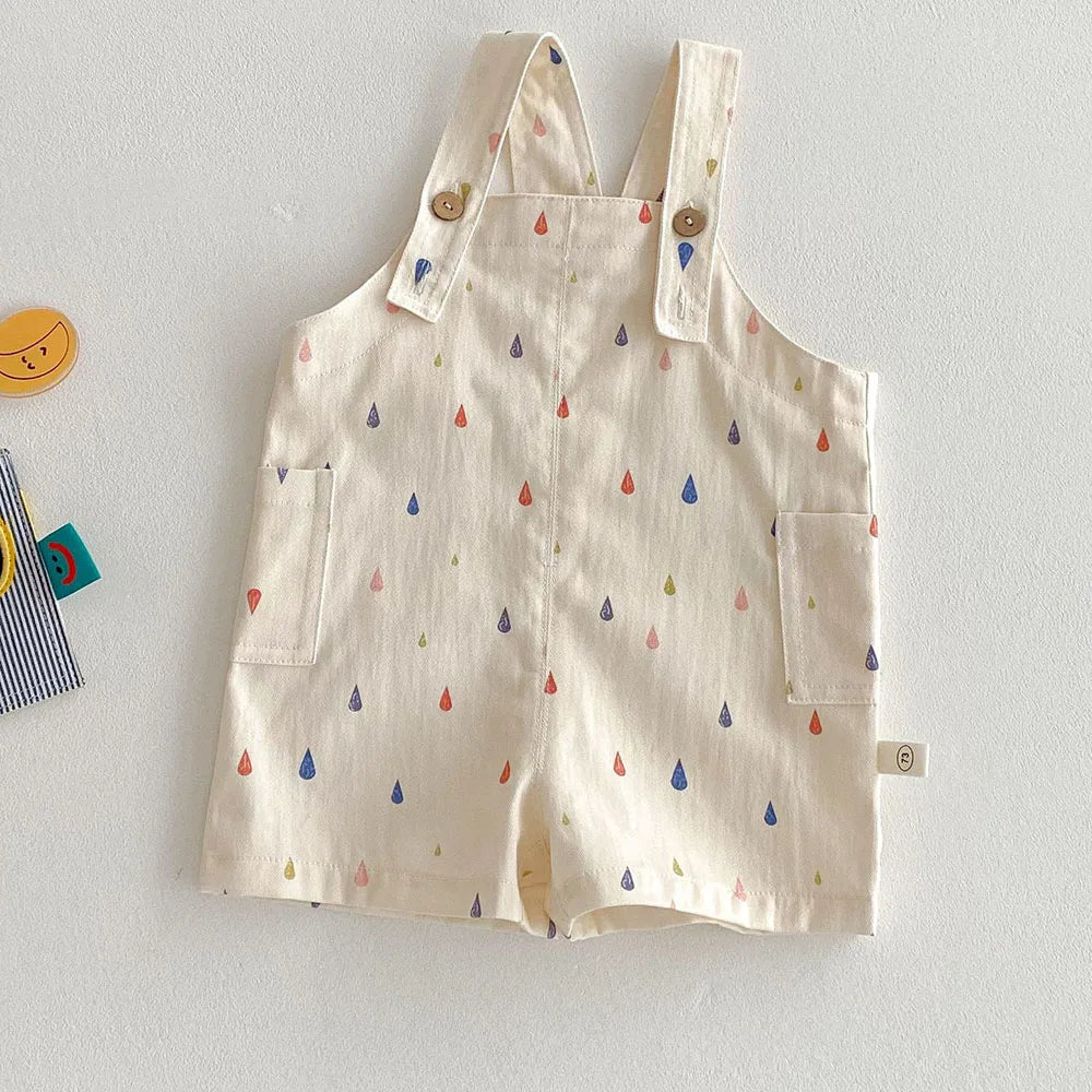 Cream colored kids overalls with a colorful raindrop print and wooden buttons