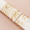 A collection of 11 gold and crystal bracelets featuring heart and infinity signs stacked on a white wrist.