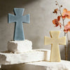 A light blue silicone cross mold sits on a white base next to a pale yellow cross mold.