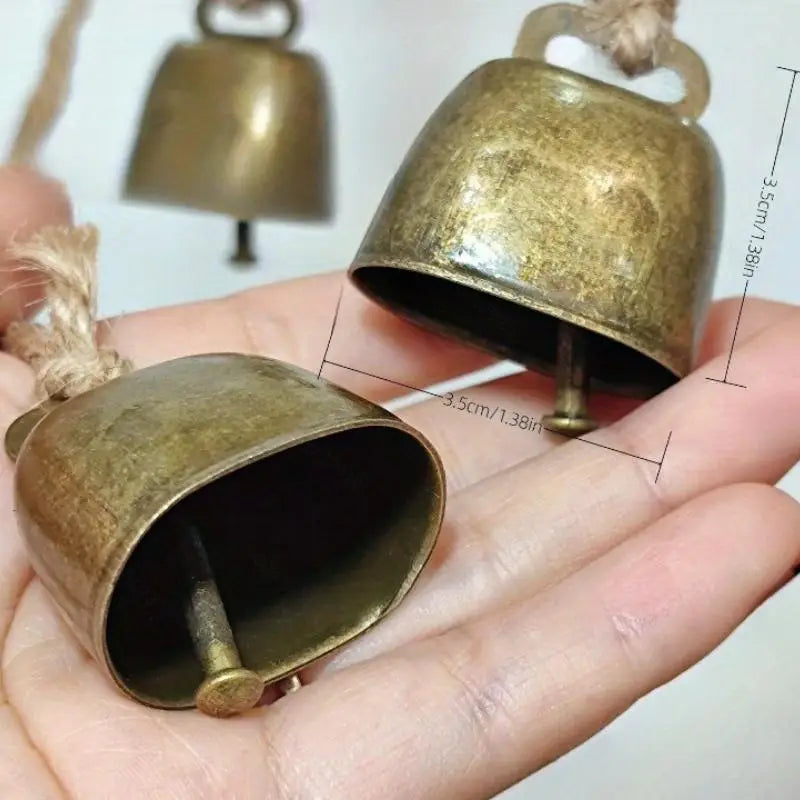 A hand holds a rustic copper jingle bell with a hemp rope, showing its size and texture.