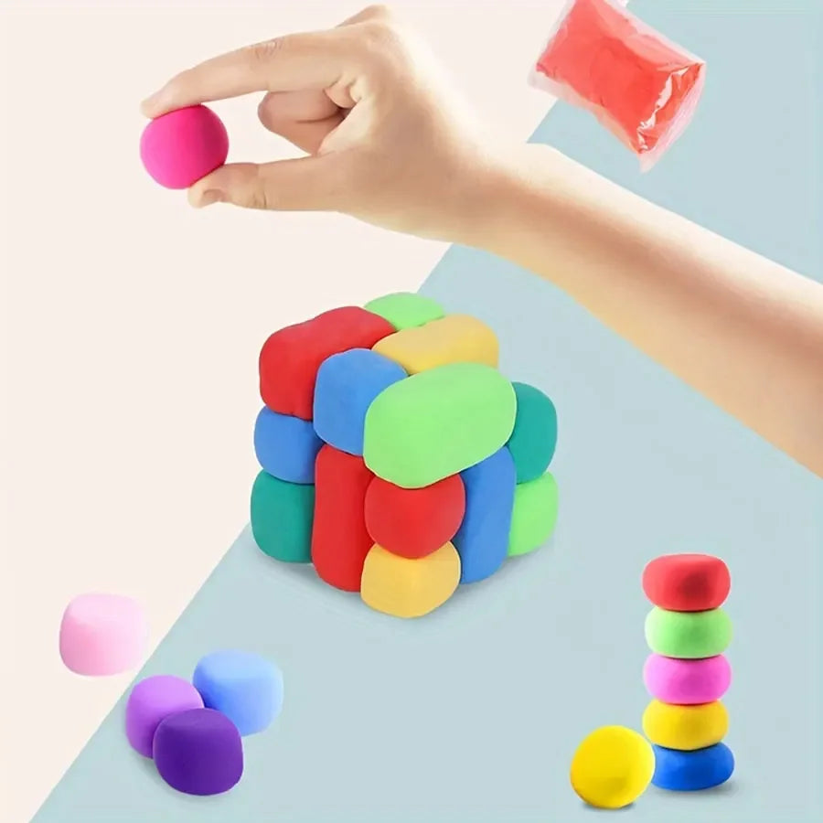 A hand holds a pink clay piece, with various colored air-dry clay pieces and tools scattered on a light blue surface.