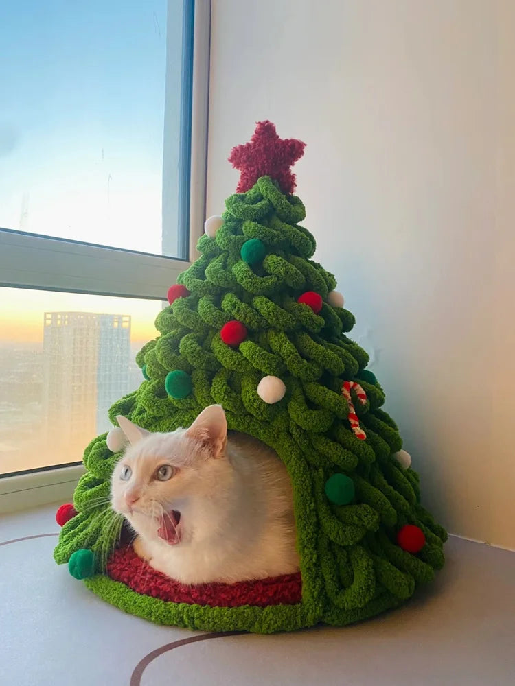 A white cat peeking out of a green knitted Christmas tree made from chunky yarn.