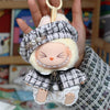 A handmade doll wearing a gray grid cape and beret set with white fur trim and pearl accents.