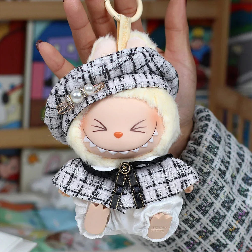 A handmade doll wearing a gray grid cape and beret set with white fur trim and pearl accents.