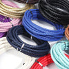 A collection of round braided leather cords in various colors including purple, pink, gold, blue, black, and white.