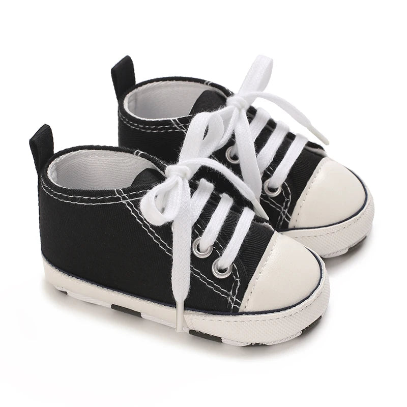 A pair of black canvas first walkers for infants with white laces and soles.