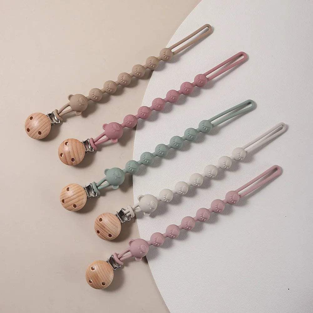 A set of silicone pacifier clips featuring bear paw shapes in various pastel colors like pink, green, and beige.