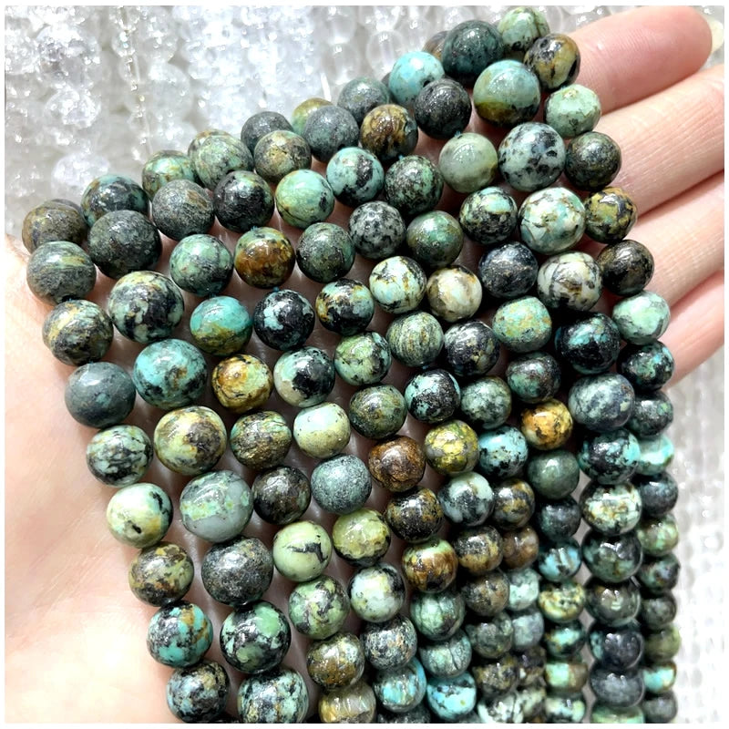 A close-up of natural stone beads in various shades of green, blue, and gray stacked on a hand.
