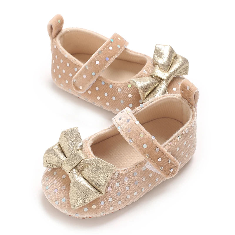 Pair of light pink soft cotton baby walking shoes with gold bow details and dotted accents