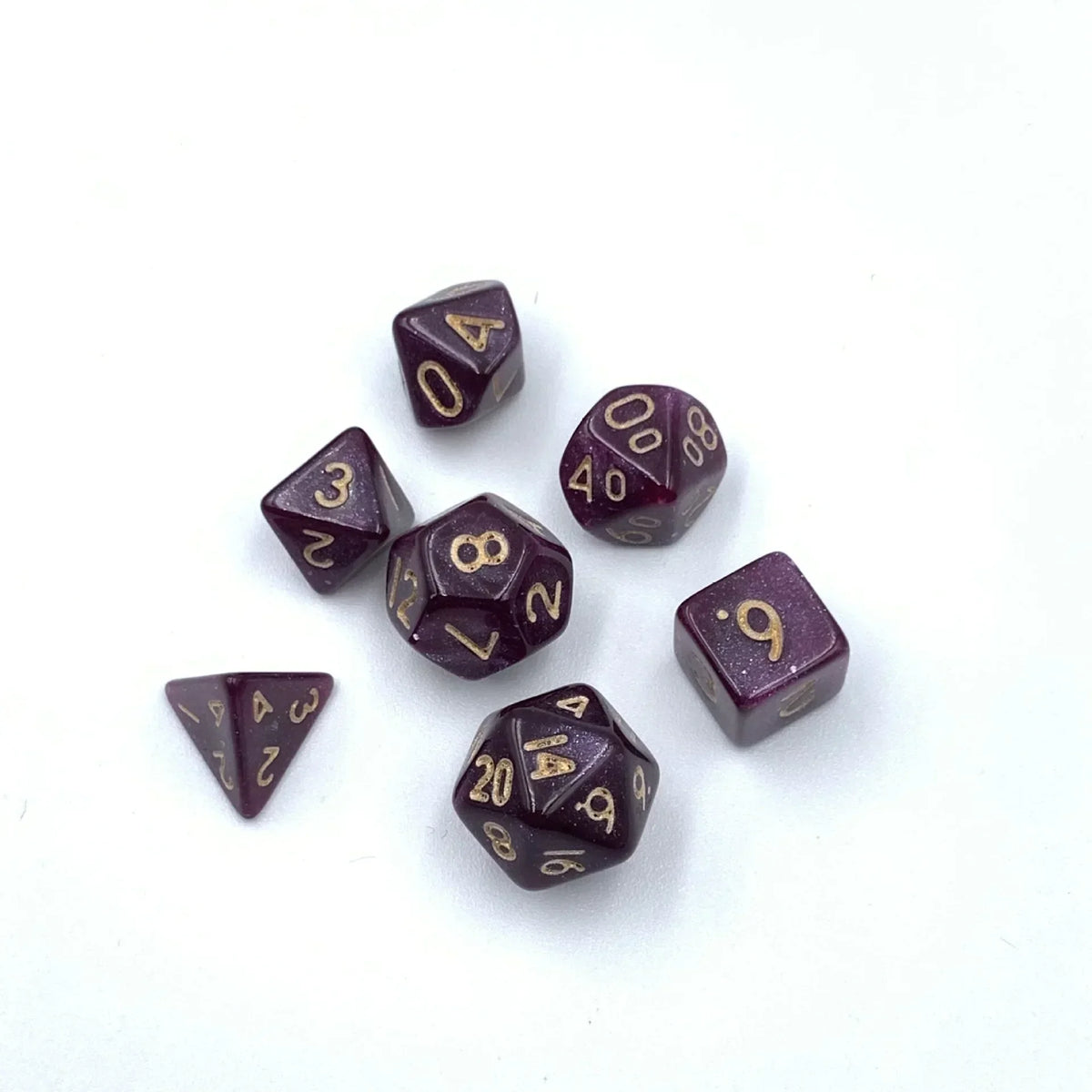 A collection of seven mini polyhedral dice in dark purple or maroon color scattered on a white background.