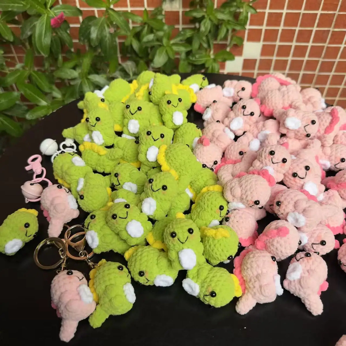 A pile of handmade crochet dinosaur keychains in various shades of green and pink.