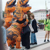 A person is hugging an inflatable orange T-Rex costume for adults outdoors.