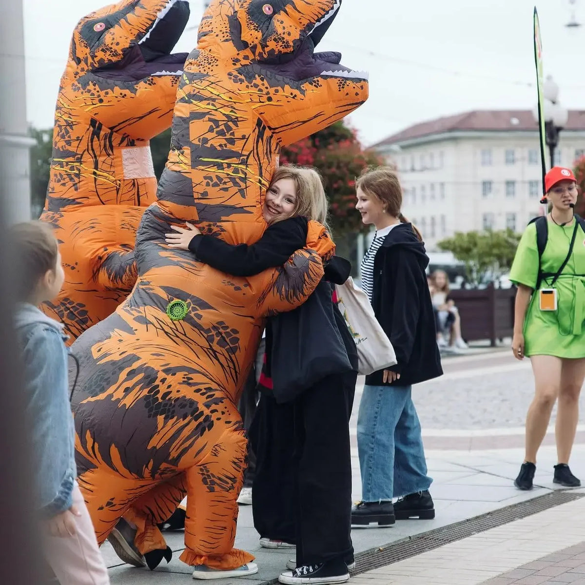A person is hugging an inflatable orange T-Rex costume for adults outdoors.