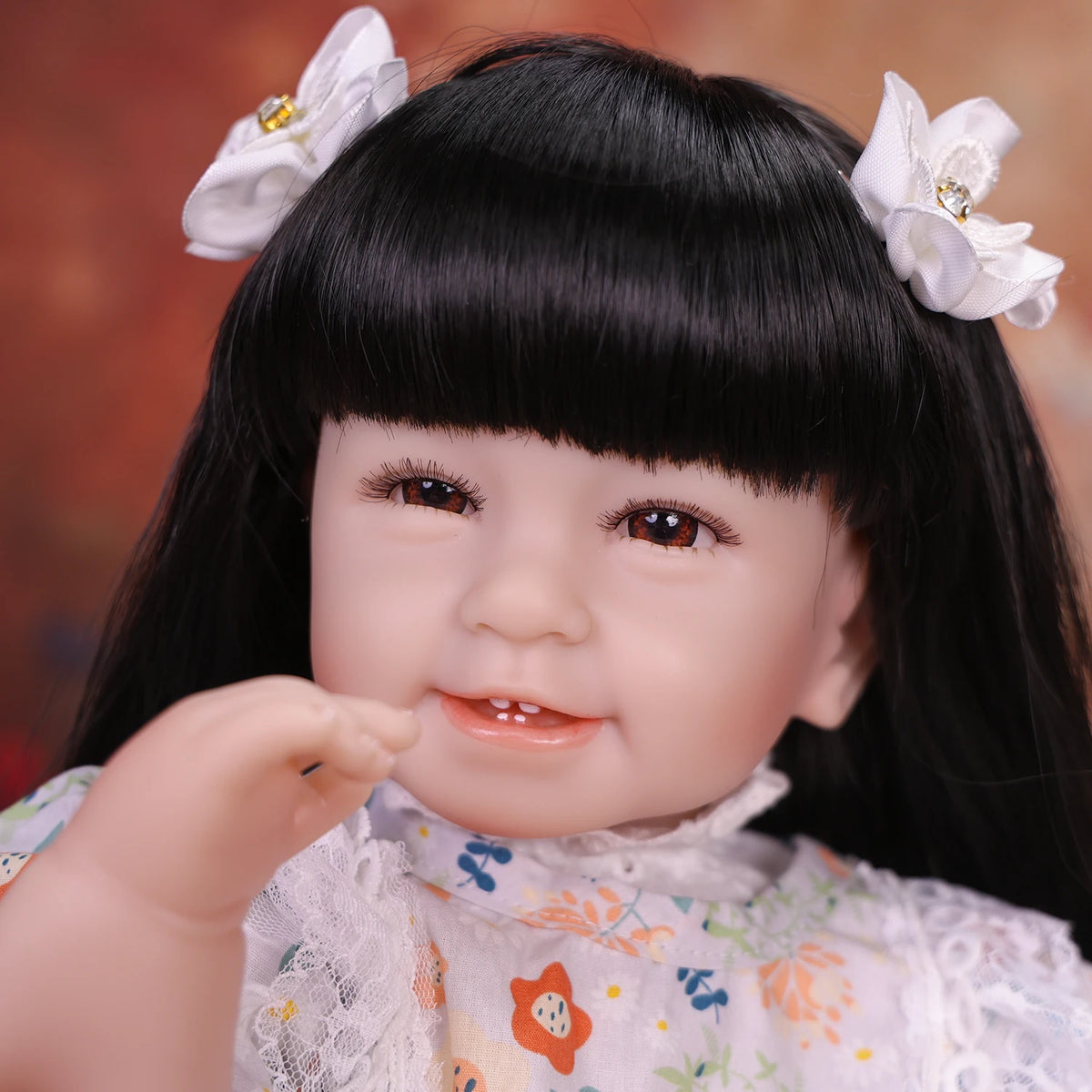 A close-up of a lifelike reborn baby doll with soft cloth body featuring black hair and white floral accessories.