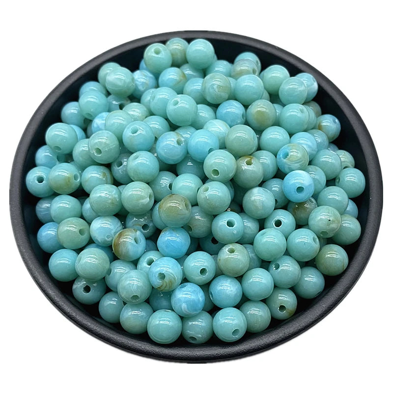 A pile of light blue and greenish-blue acrylic round beads for jewelry making.