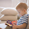 A toddler sits on a couch looking at a soft sensory cloth book for babies with crinkle pages.