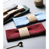 A set of folded linen napkins in various shades of blue, green, and burgundy resting on a gray surface.