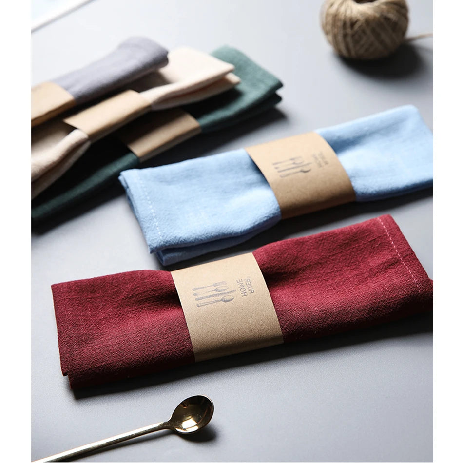 A set of folded linen napkins in various shades of blue, green, and burgundy resting on a gray surface.