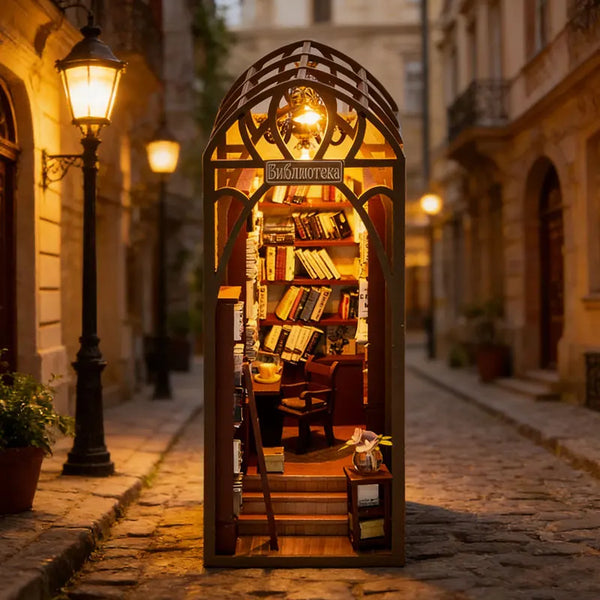 A wooden miniature dollhouse kit displayed in a decorative arched frame on a cobblestone street.