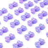 A scattering of iridescent purple acrylic bow beads for jewelry making.