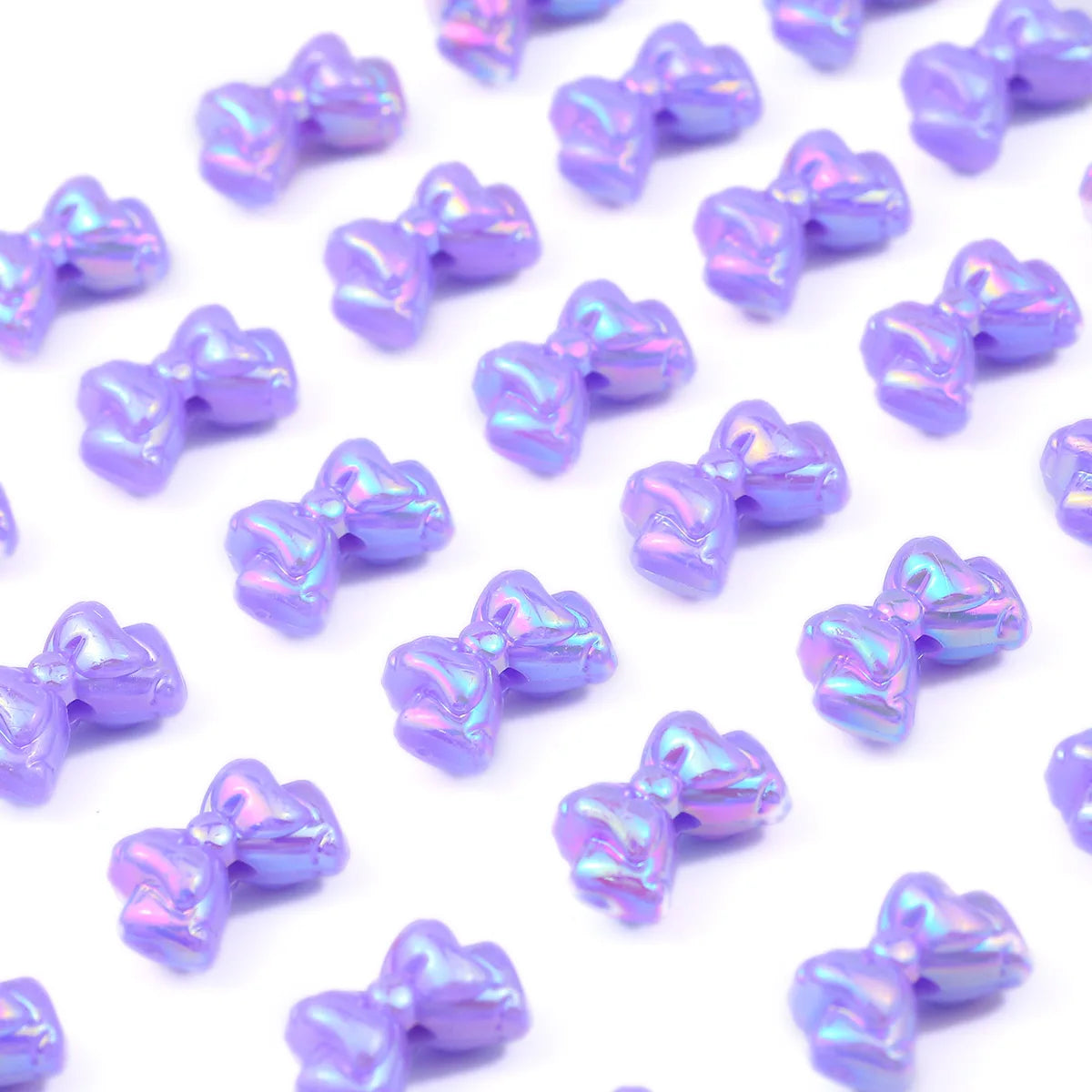 A scattering of iridescent purple acrylic bow beads for jewelry making.