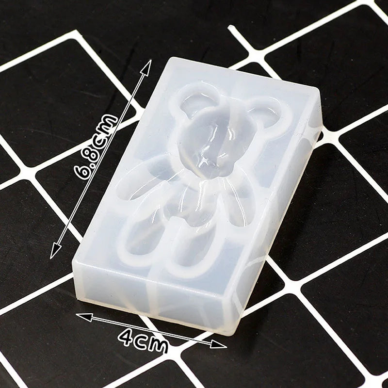 A clear silicone mold shaped like a bear, used for resin jewelry and crafts, shown on a grid background.