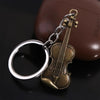 A vintage violin-shaped keychain with a silver ring and brass hardware resting on a dark surface.