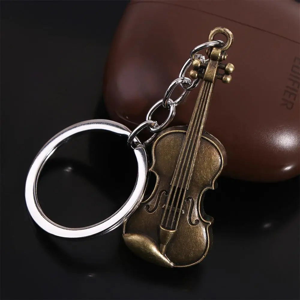 A vintage violin-shaped keychain with a silver ring and brass hardware resting on a dark surface.