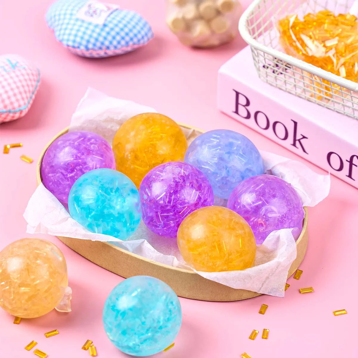 A collection of six colorful, translucent soft squeeze balls in purple, yellow, and blue resting on pink surfaces.