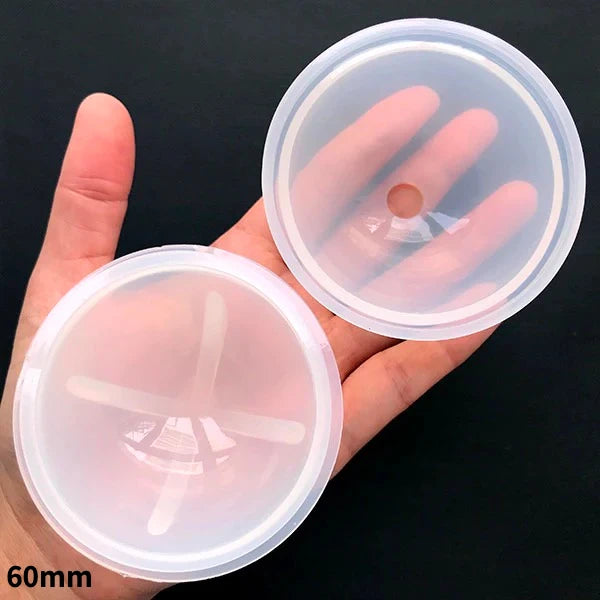 A hand holds two clear silicone molds for resin crafting, showing the circular shape and texture.