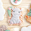 A white silicone baking mold shaped like a cute elephant is shown surrounded by other decorative molds on a wooden surface.