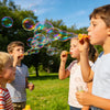 Three children blowing bubbles outdoors in a sunny park setting