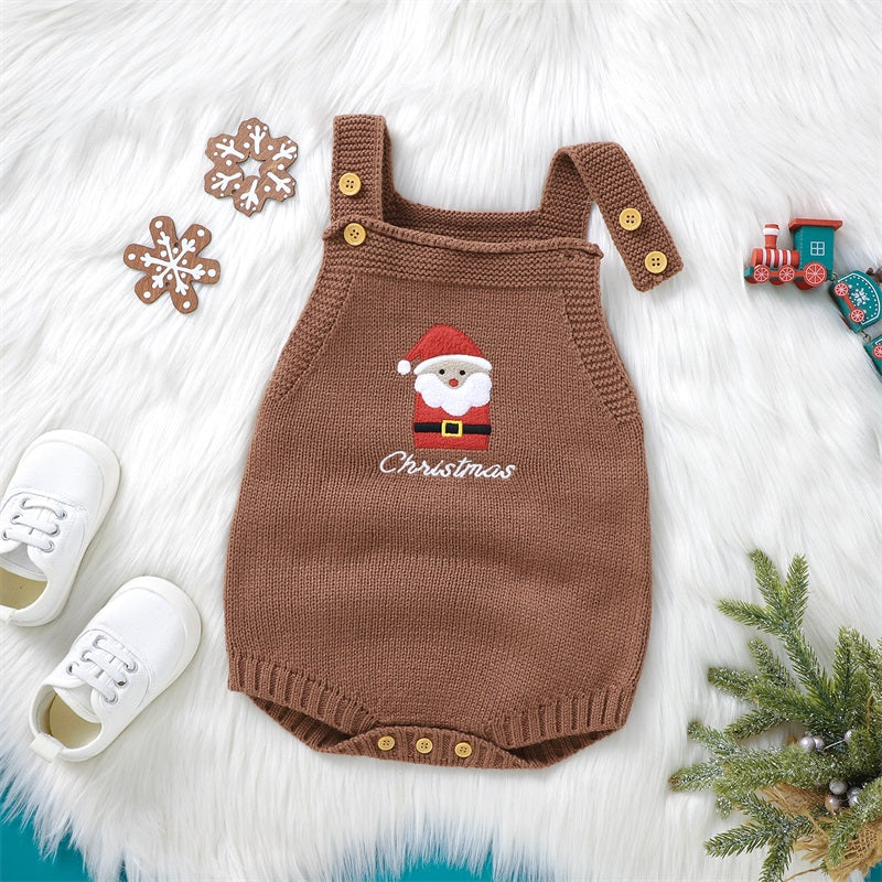 A brown knit baby romper embroidered with a Santa face is displayed on white fur, with matching shoes nearby.