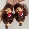 A pair of brown Monchhichi plush toys are shown hanging from a keychain, with a red tag visible.