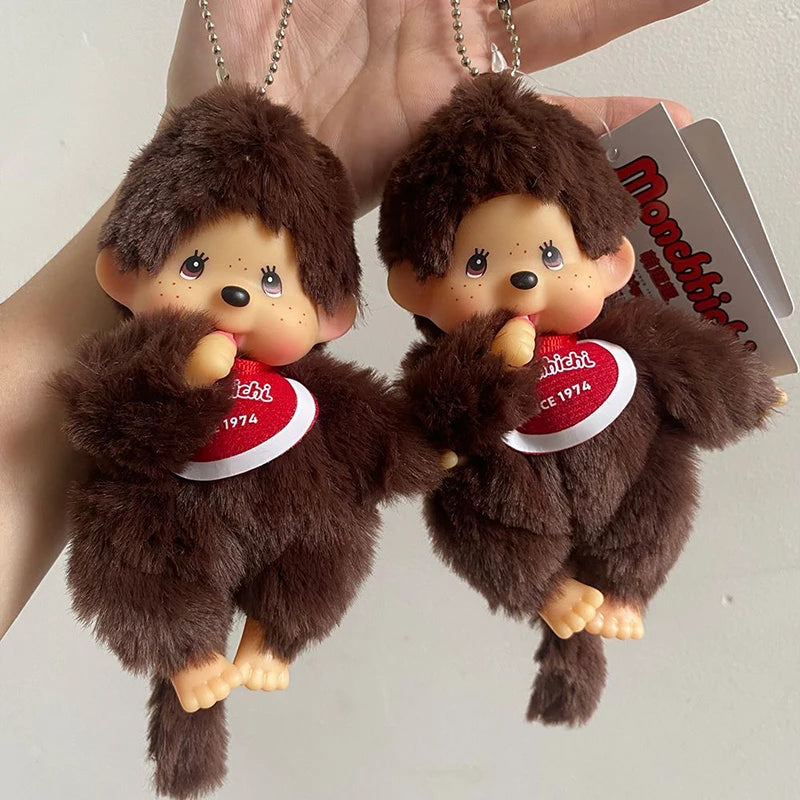 A pair of brown Monchhichi plush toys are shown hanging from a keychain, with a red tag visible.