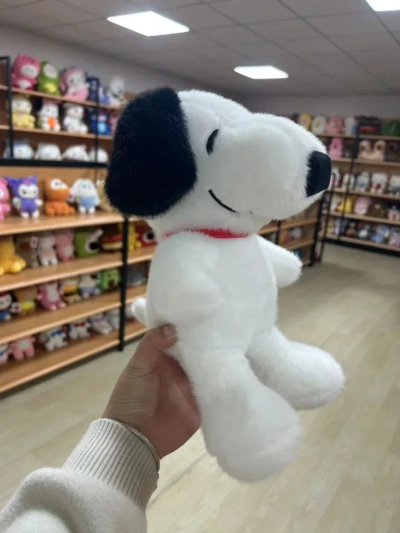 A hand is holding a white and black Snoopy cartoon plush toy with a red collar in a retail store setting.