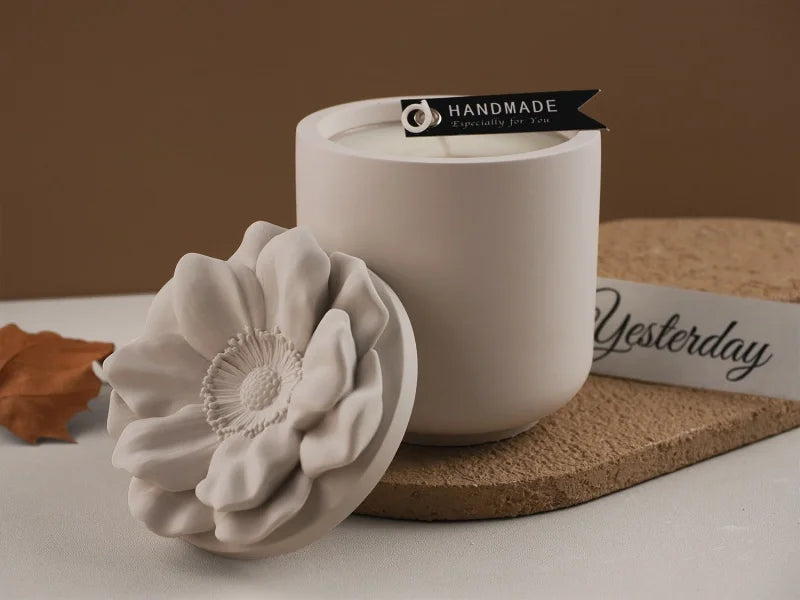 A white ceramic candle cup sits next to a large, sculpted white floral silicone mold on a beige surface.