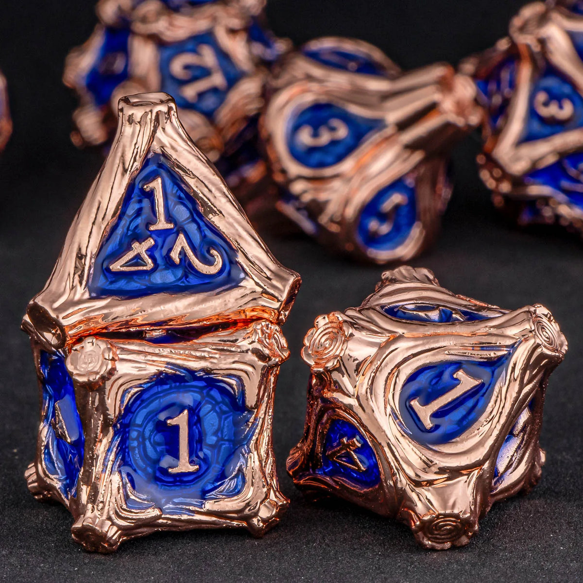 A set of seven polyhedral metal dice in gold and blue colors resting on a dark surface.